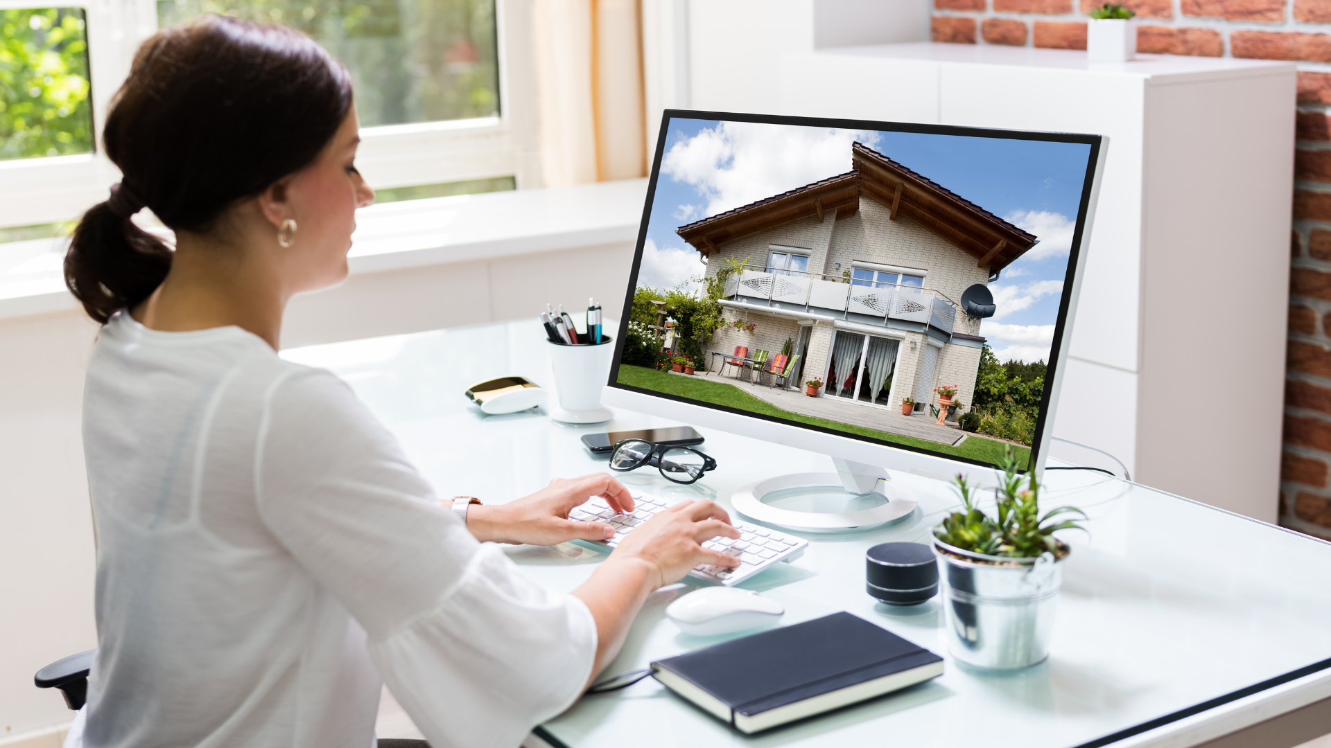Woman at desk viewing house listing on a computer screen, office setting.