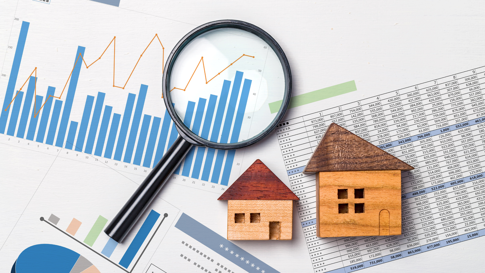 Magnifying glass over charts and two miniature houses, illustrating real estate market analysis.