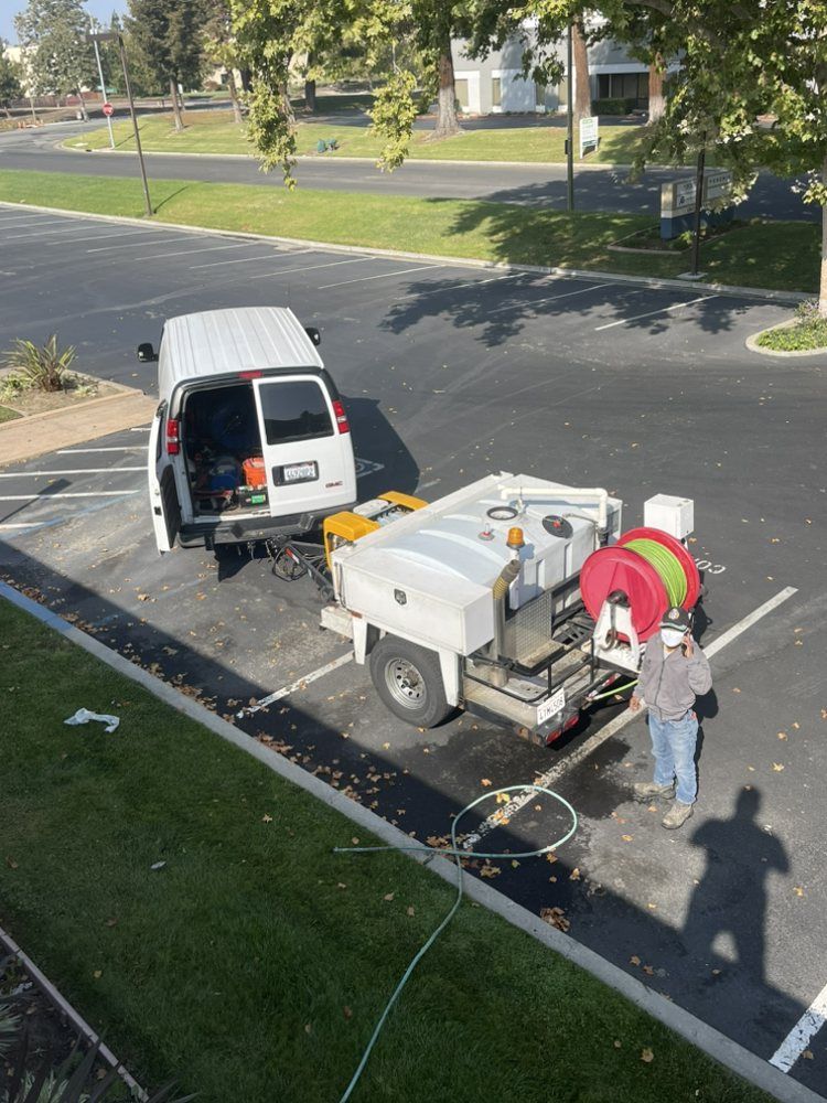 A White Van Is Parked in A Parking Lot Next to A Trailer with A Hose Attached to It – Hayward, Ca – Plumbing 1 Builders Inc.