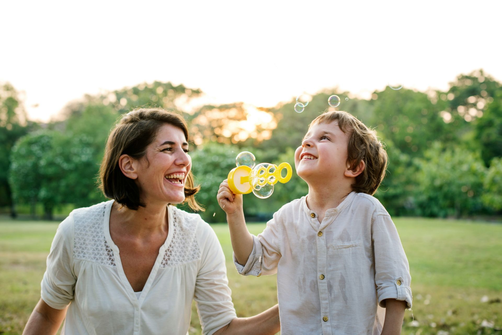 A woman and a child are blowing soap bubbles in a park.