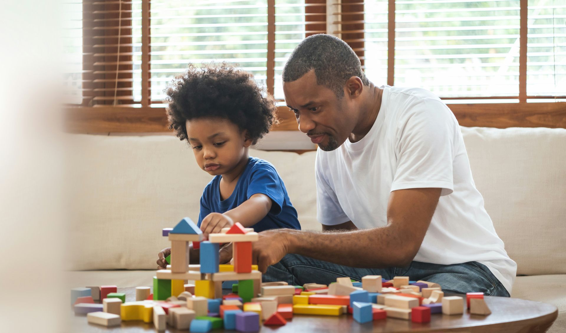 A man and a child are playing with wooden blocks on a table.