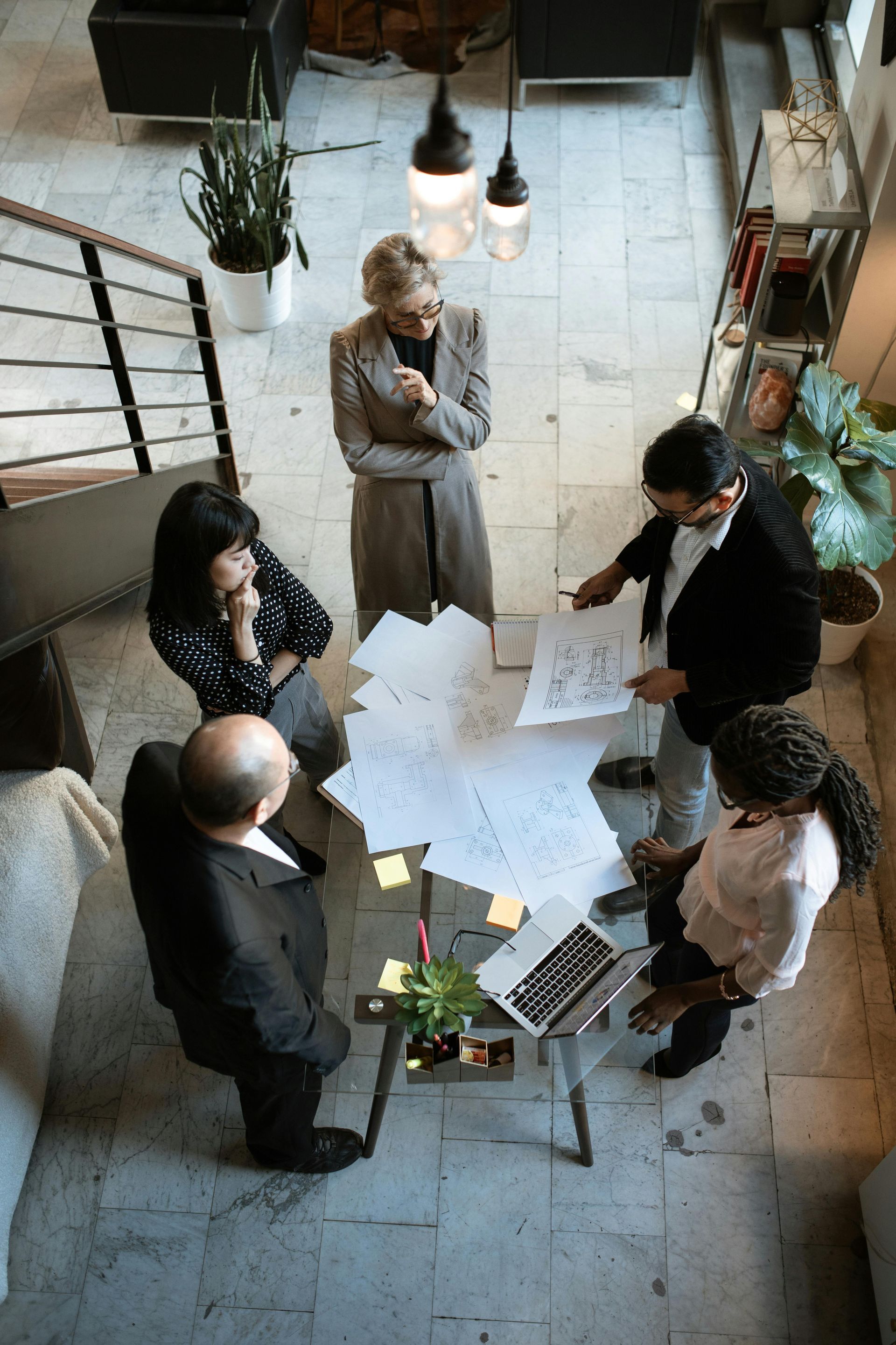 A diverse team in a meeting, looking at papers and a laptop around a small table. Overhead view.