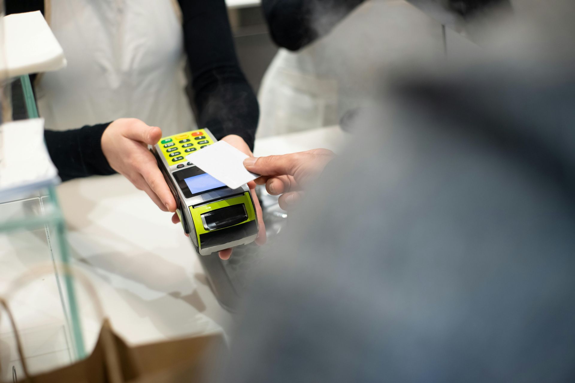 Person paying with card at a point-of-sale terminal. Hands interacting, setting is a store counter.