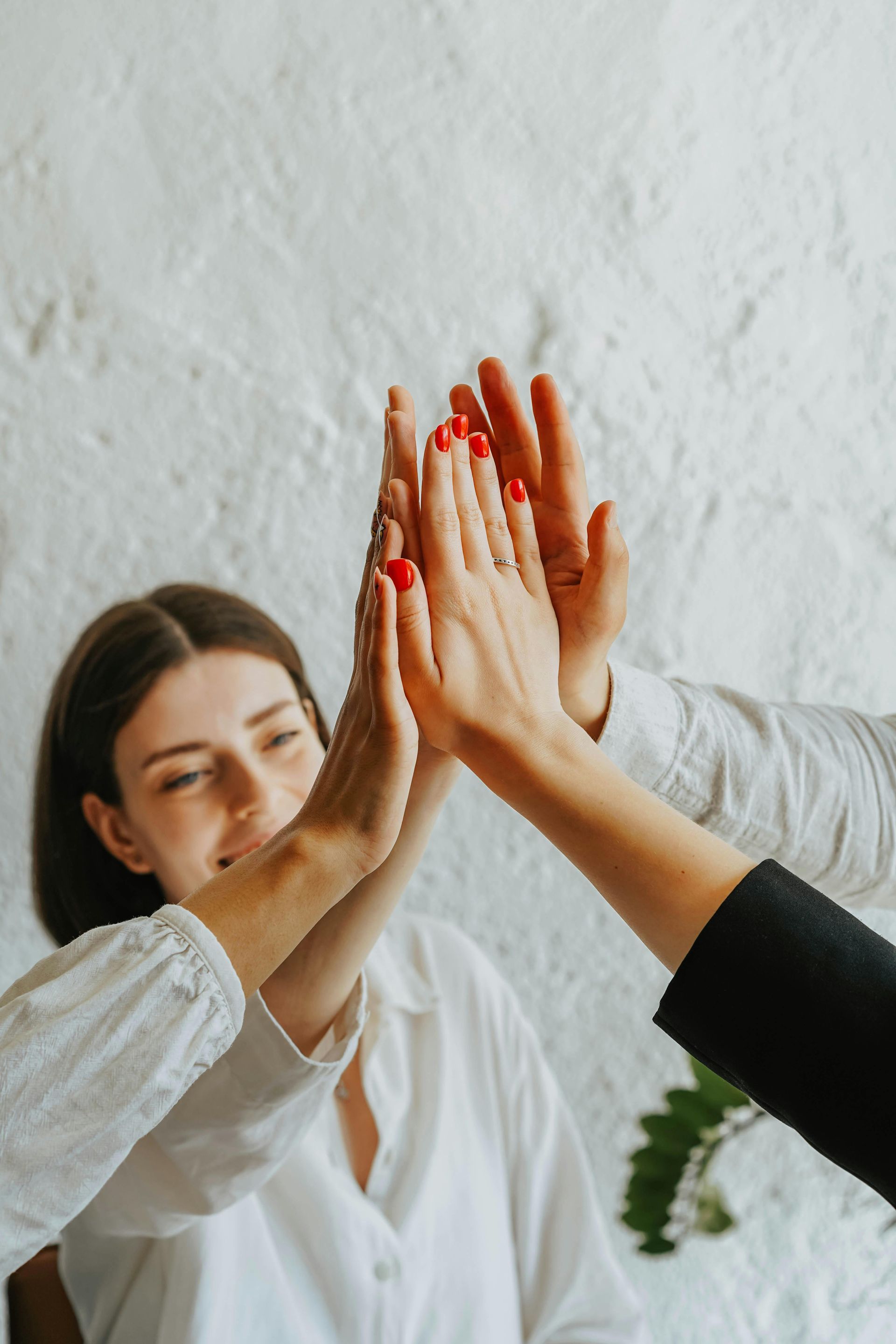 Hands giving a high five, woman smiles, white shirts, white textured wall.