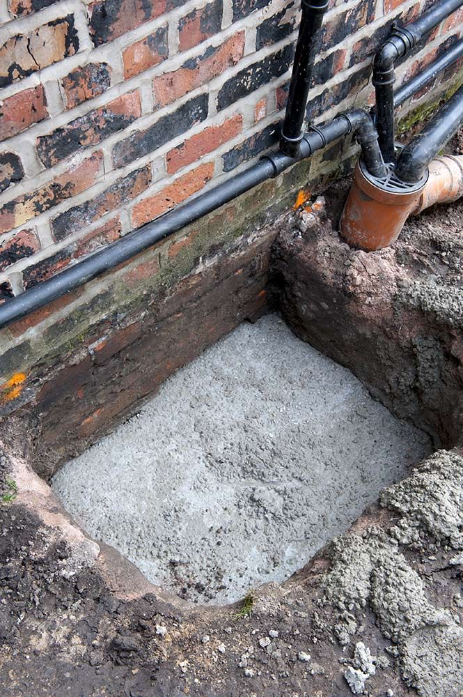 A Hole in the Ground Next to a Brick Wall With Pipes Coming Out of It — Knobel Builders In Balgownie, NSW