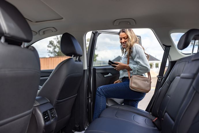 A woman is sitting in the back seat of a car looking at her phone.