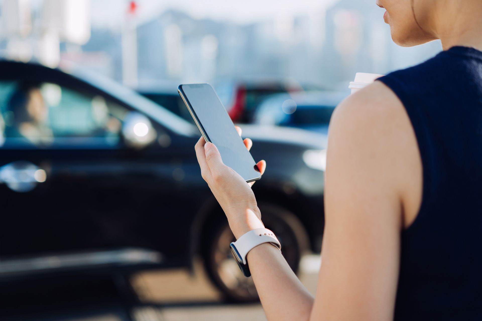 A woman is holding a cell phone in front of a car.