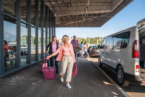 Tourists, dragging suitcases towards a white van at the airport, for a group airport transfer.
