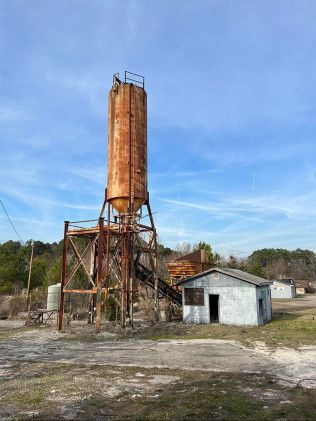 There is a large rusty silo in the middle of a field.