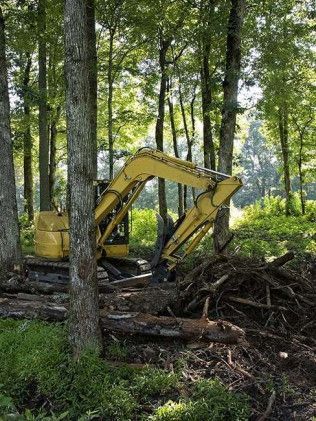 A yellow excavator is sitting in the middle of a forest.