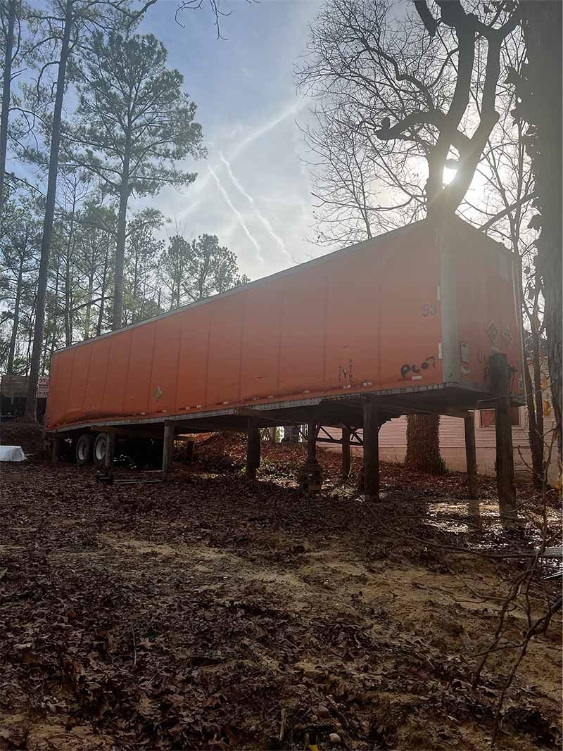 A large orange trailer is parked in the middle of a forest.
