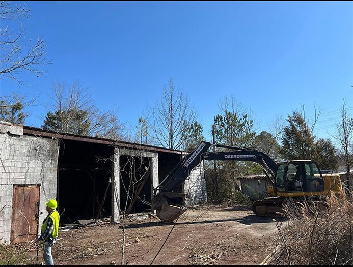 A man in a yellow vest is standing in front of an excavator.