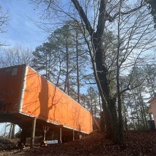 An orange trailer is sitting in the middle of a forest.