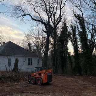 A bulldozer is sitting in a dirt field in front of a house surrounded by trees.