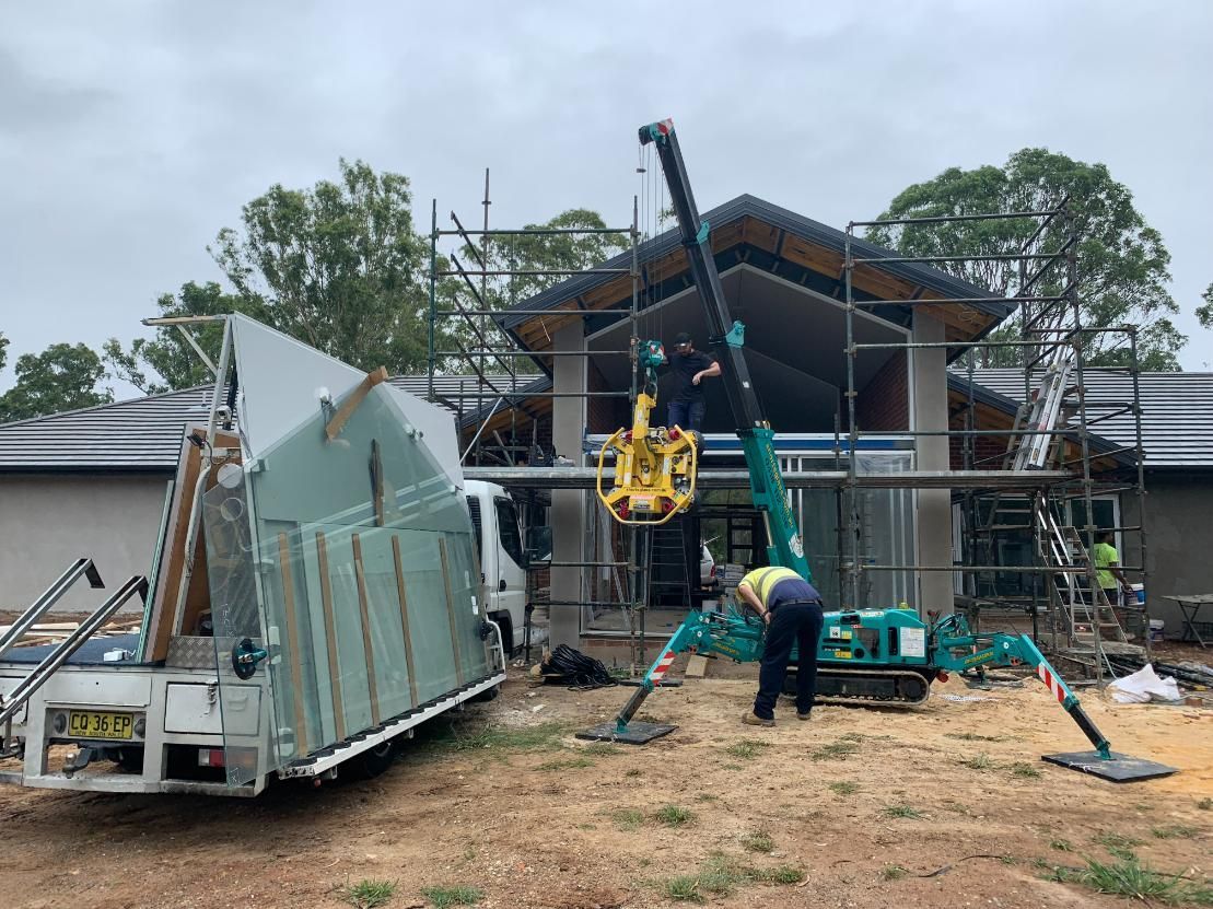 A Crane Is Lifting A Large Piece Of Glass In Front Of A House Under Construction — Central Coast Glass & Glazing In Umina Beach, NSW