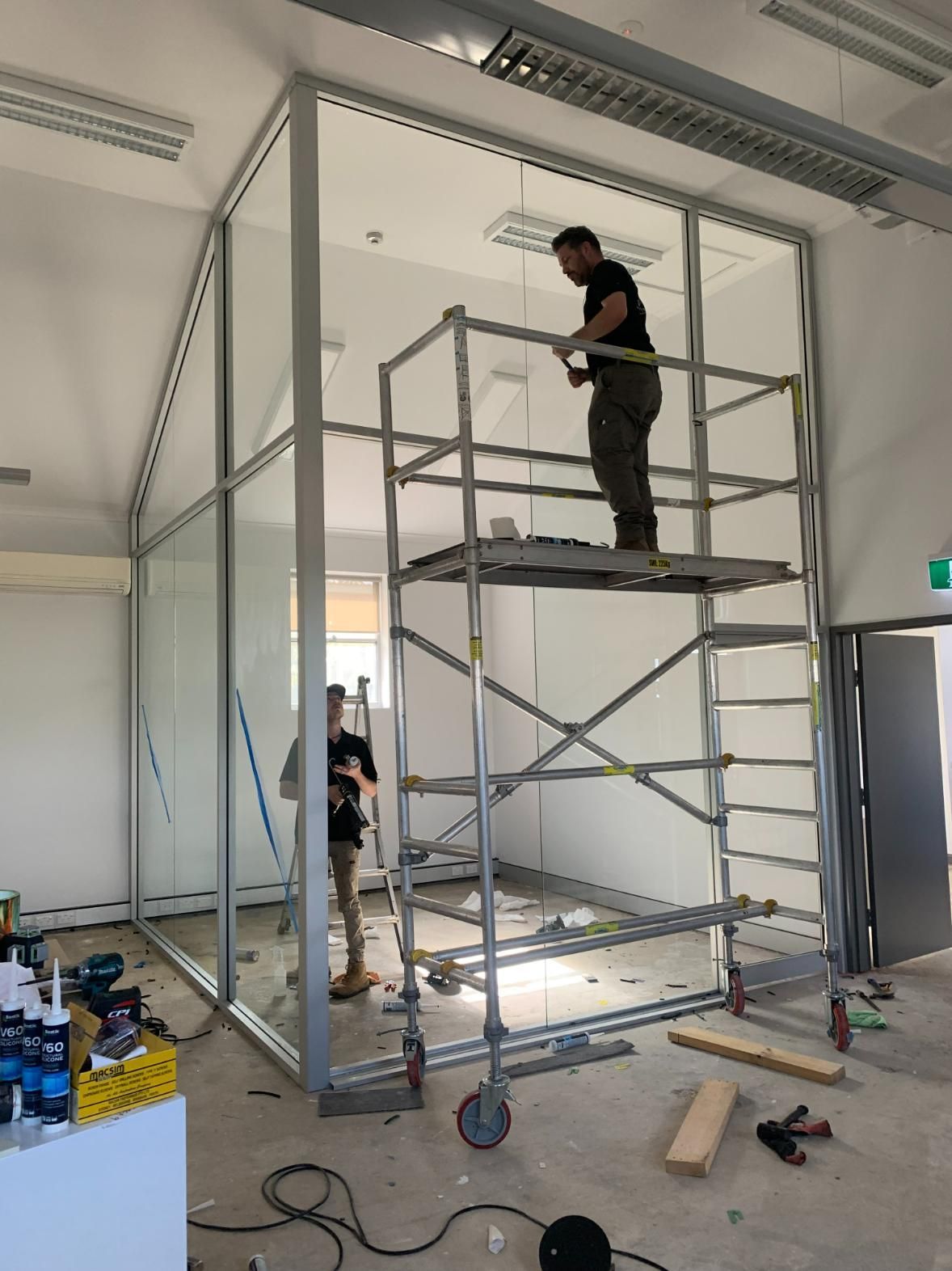 A Man Is Standing On A Scaffolding In A Room — Central Coast Glass & Glazing In Umina Beach, NSW