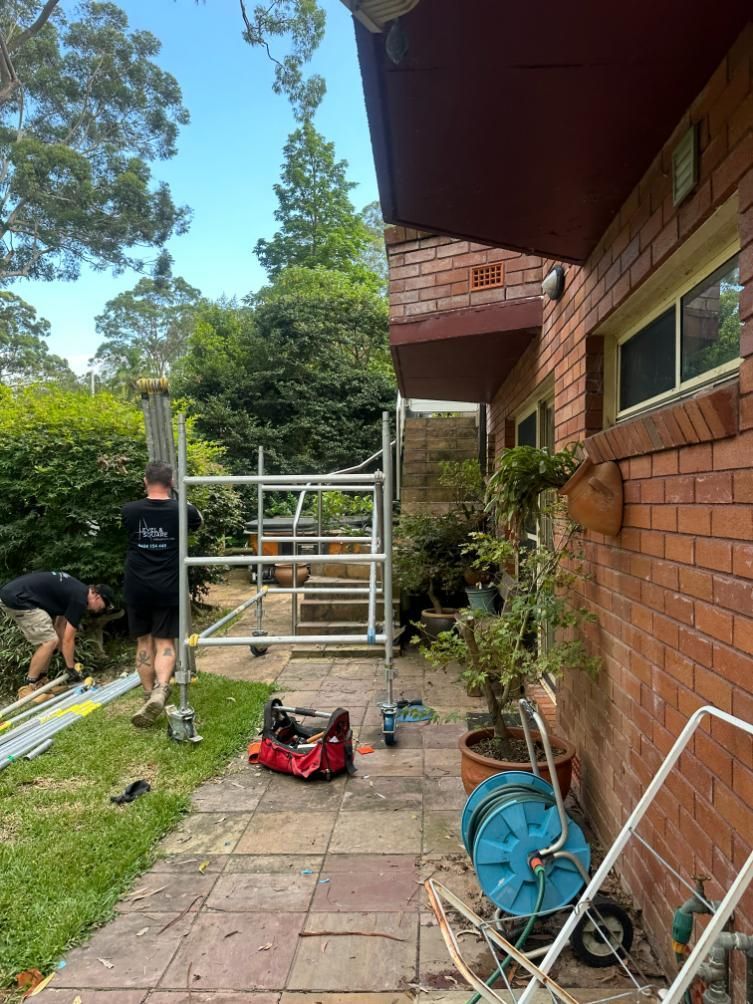 A Man Is Standing On A Scaffolding In Front Of A Brick Building — Central Coast Glass & Glazing In Erina, NSW