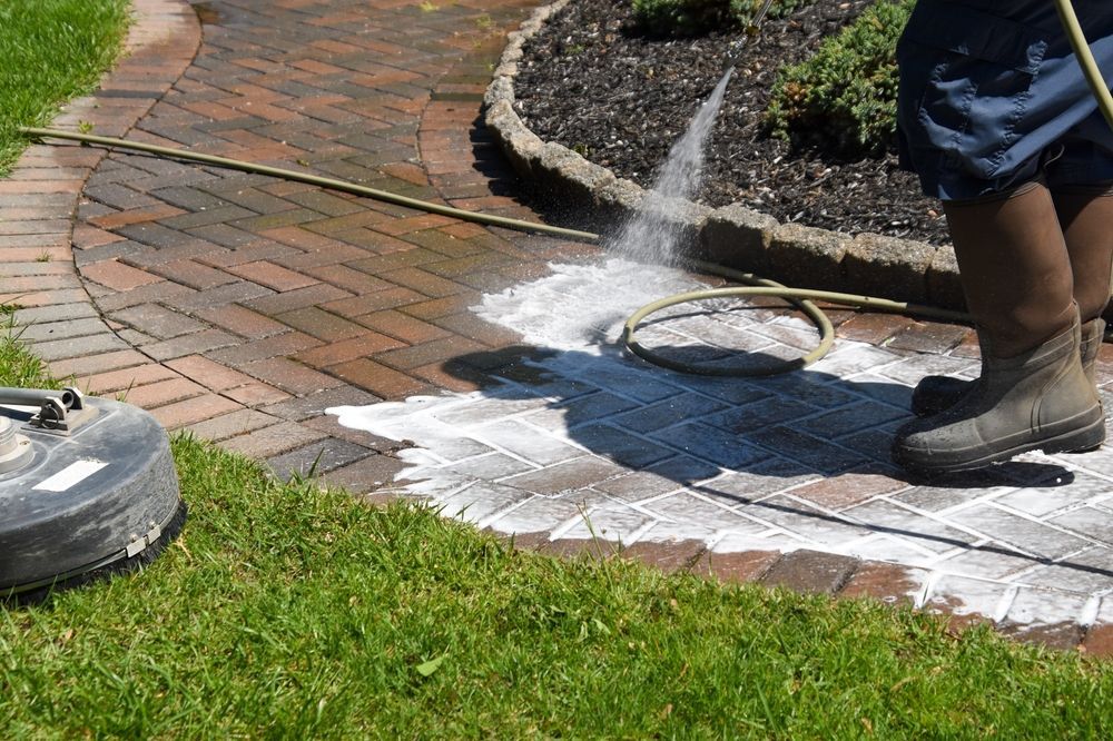 A person is cleaning a brick walkway with a pressure washer.