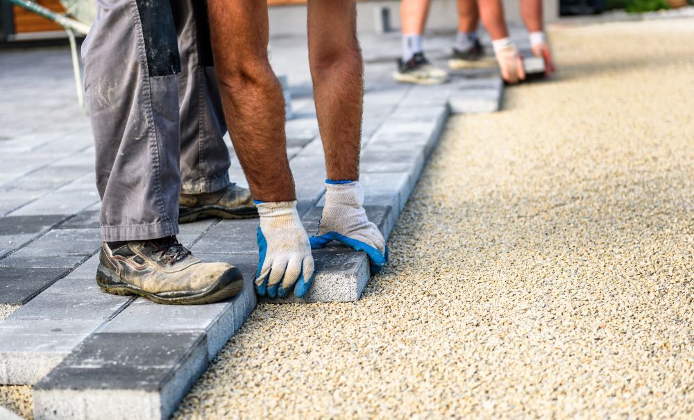 A man wearing blue gloves is laying bricks on a sidewalk.