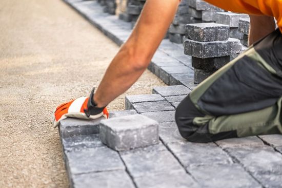 A man is kneeling down and putting bricks on a sidewalk.