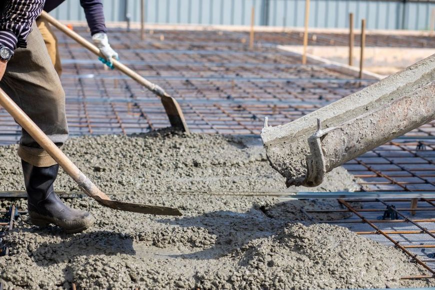 A man is pouring concrete into a foundation with a shovel.