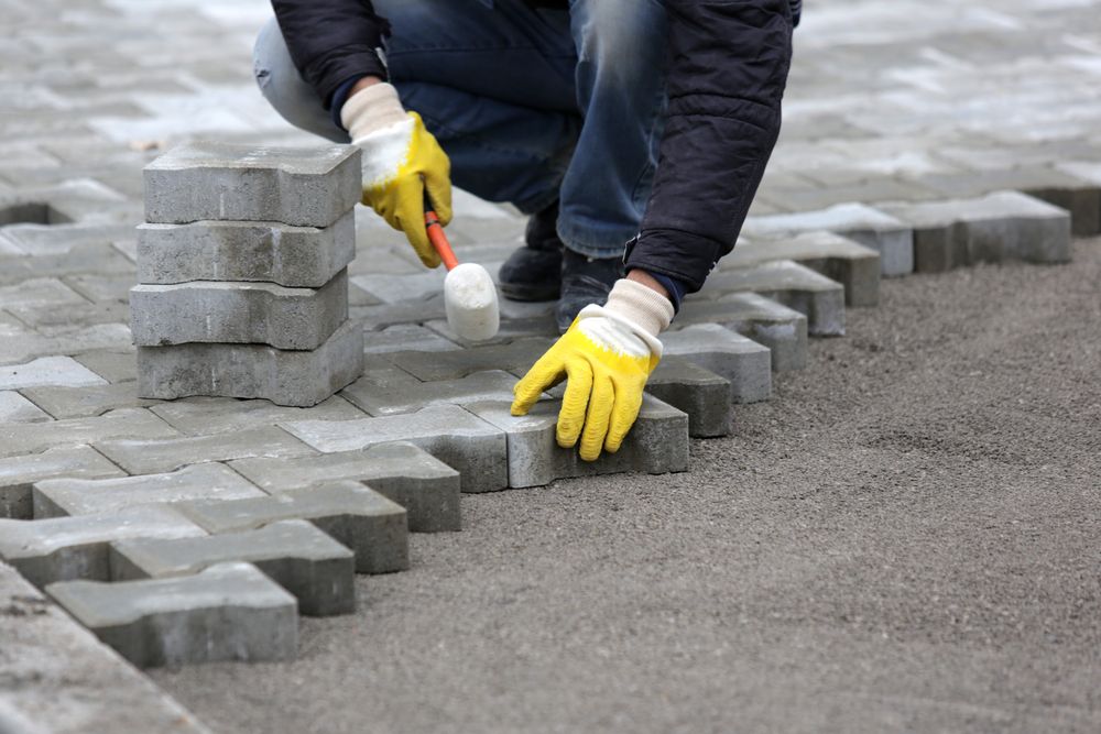 A man is laying bricks on a sidewalk with a hammer.