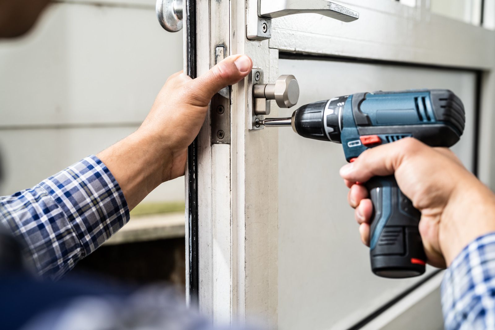 A man is using a drill to fix a door lock.