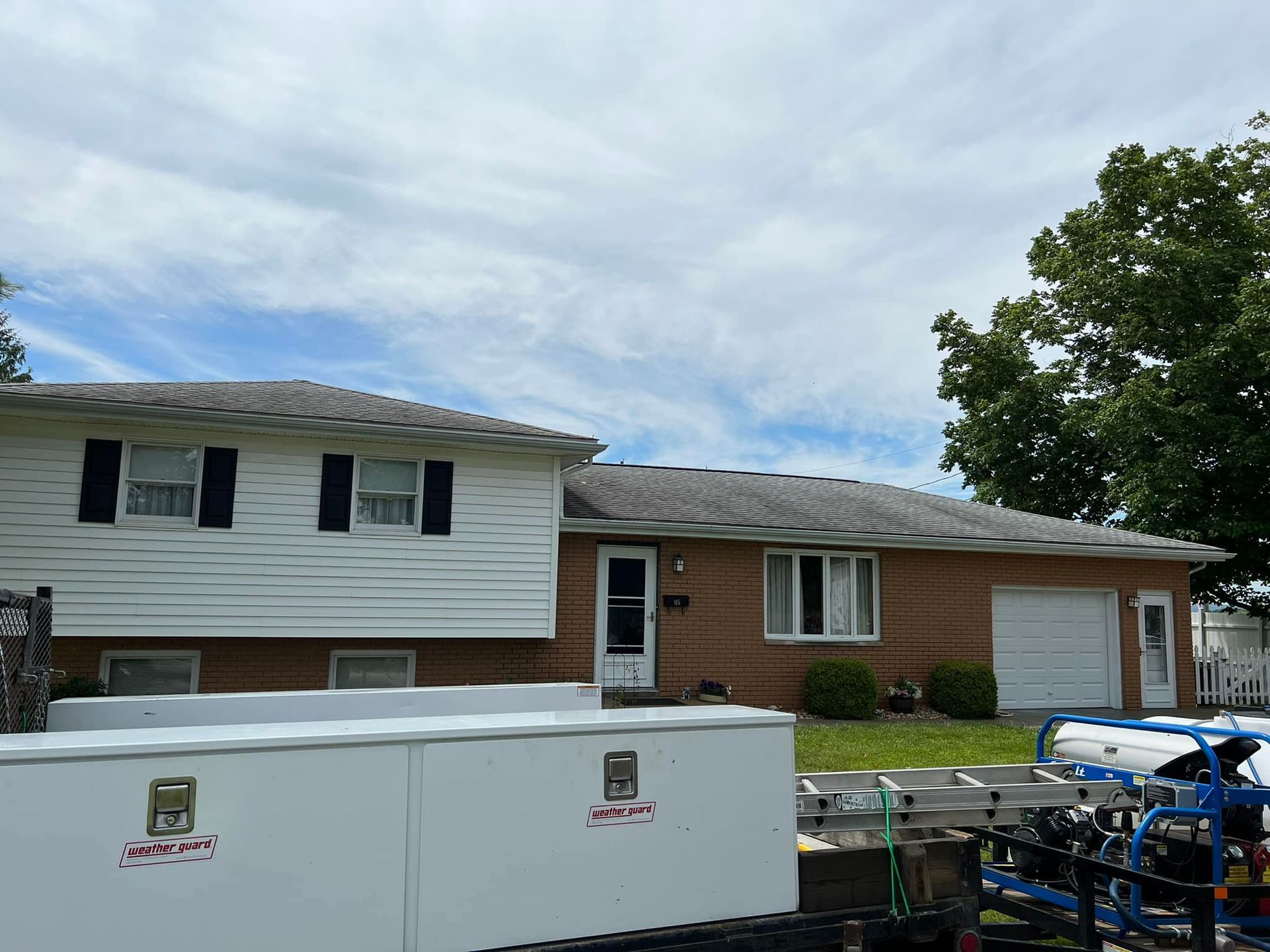 A white trailer is parked in front of a brick house.