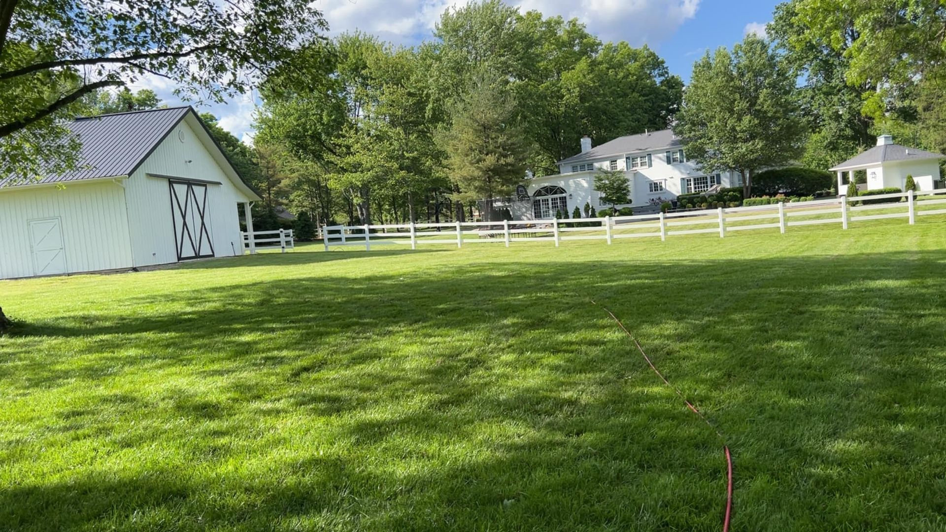 A large grassy field with a white barn and a white fence in the background.