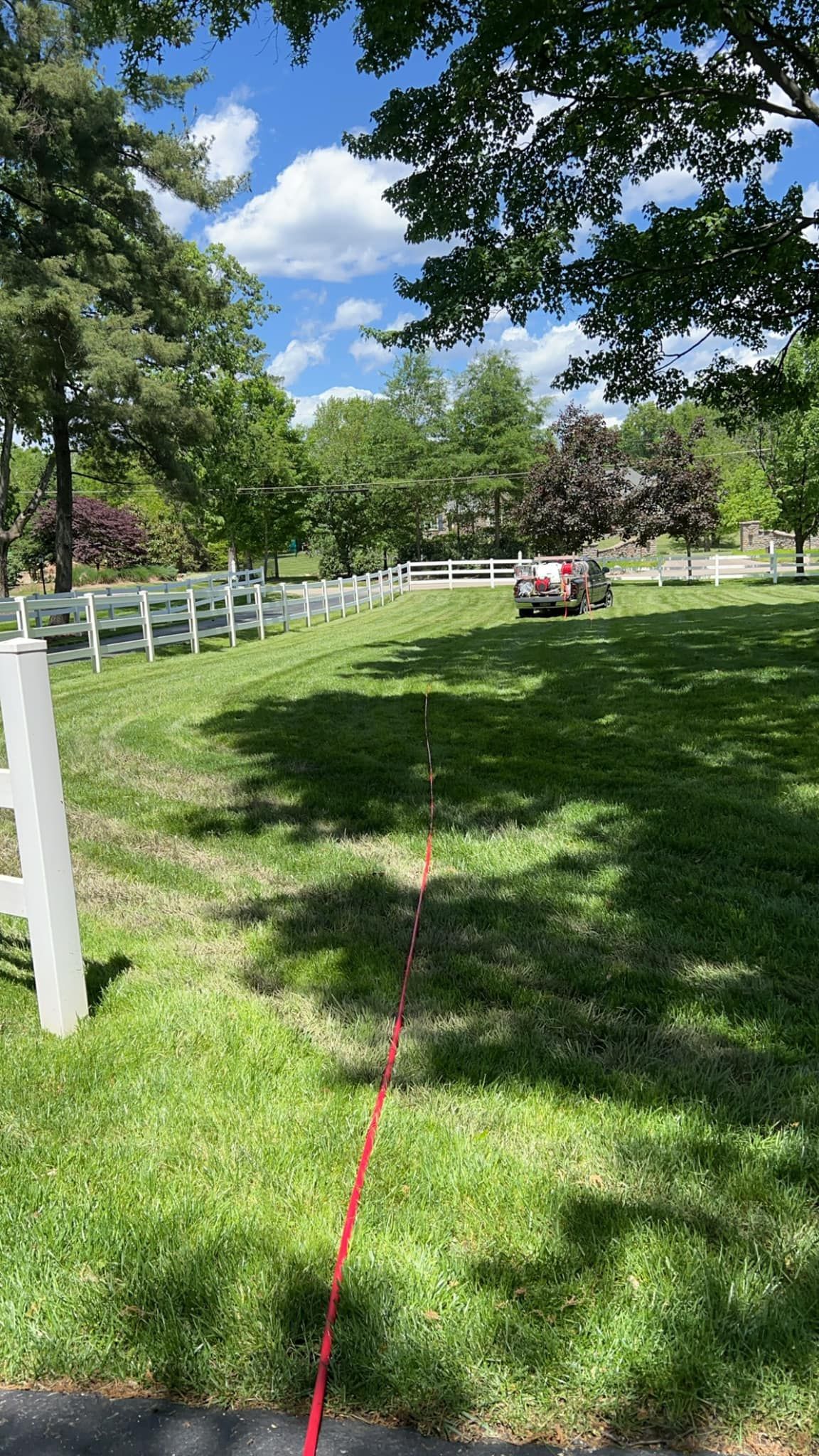 A tractor is cutting grass in a grassy field next to a white fence.