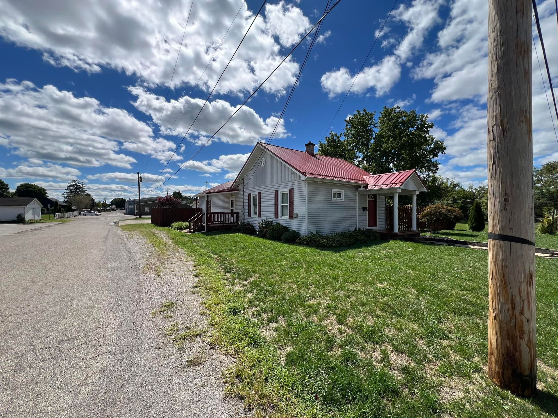 A white house with a red roof is sitting on the side of the road next to a power pole.