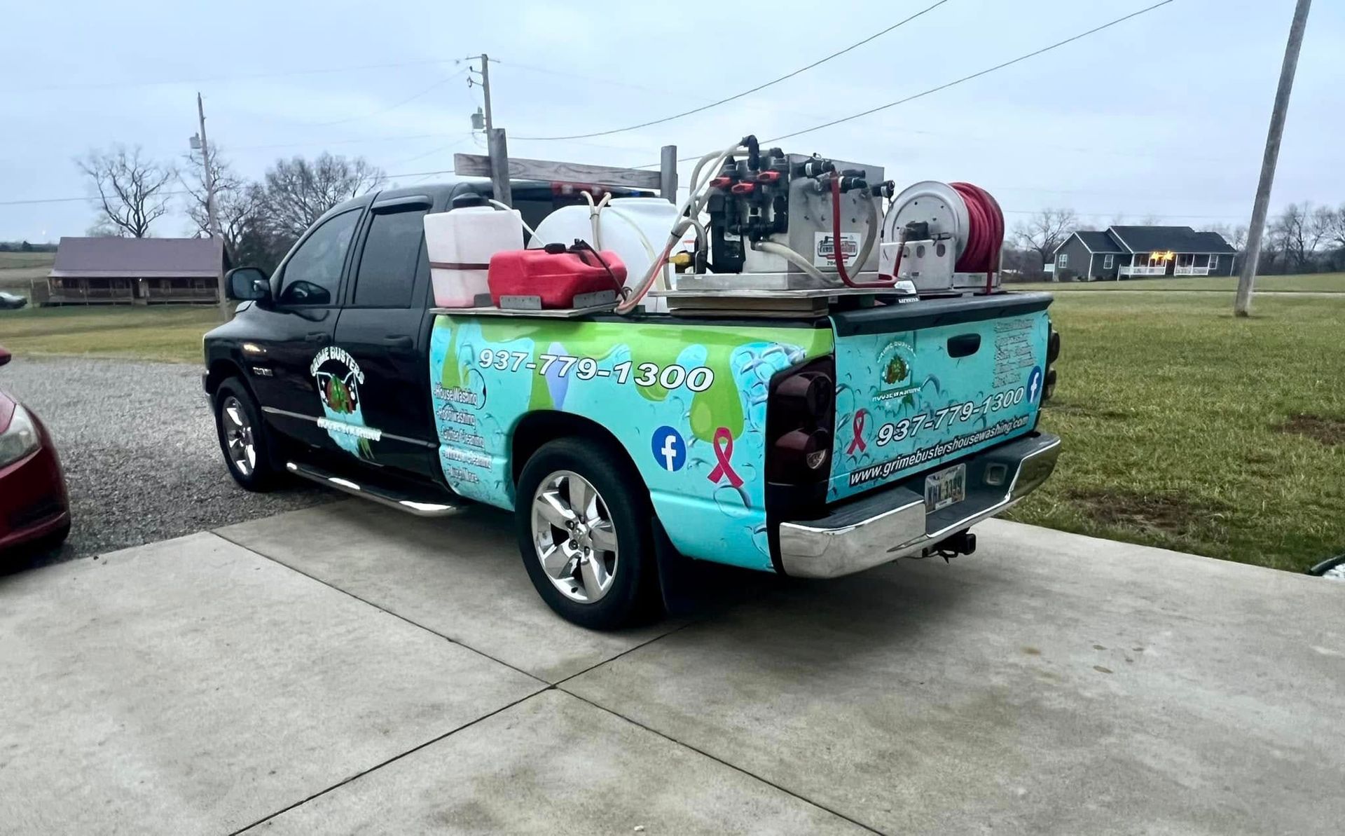 A colorful truck is parked in a driveway next to a red car.