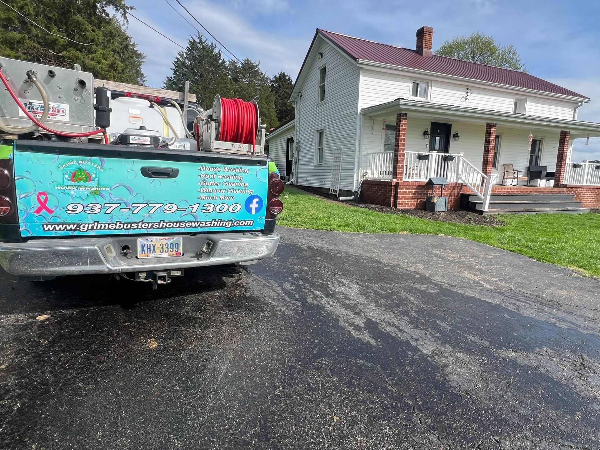 A teal work truck with cleaning equipment parked in front of a white farmhouse with a covered porch.