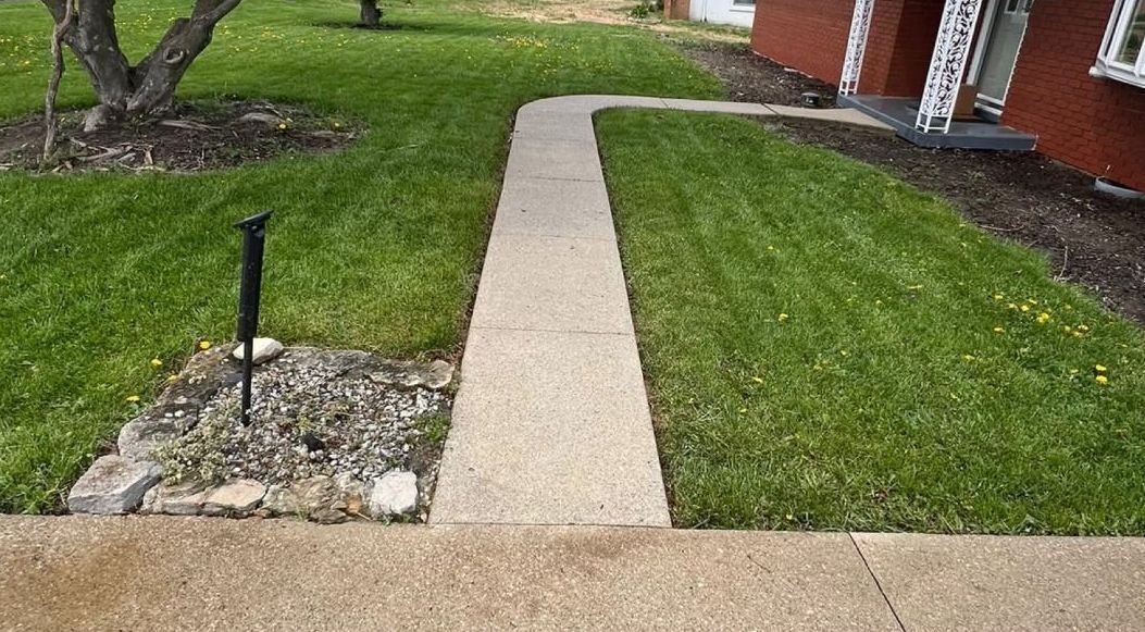 A concrete walkway leading to a house with a fence in the background.