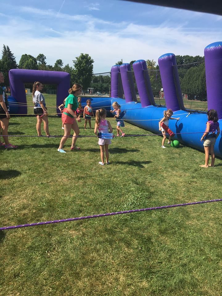 A group of children play with a ball on the grass next to a large blue and purple inflatable obstacle course.