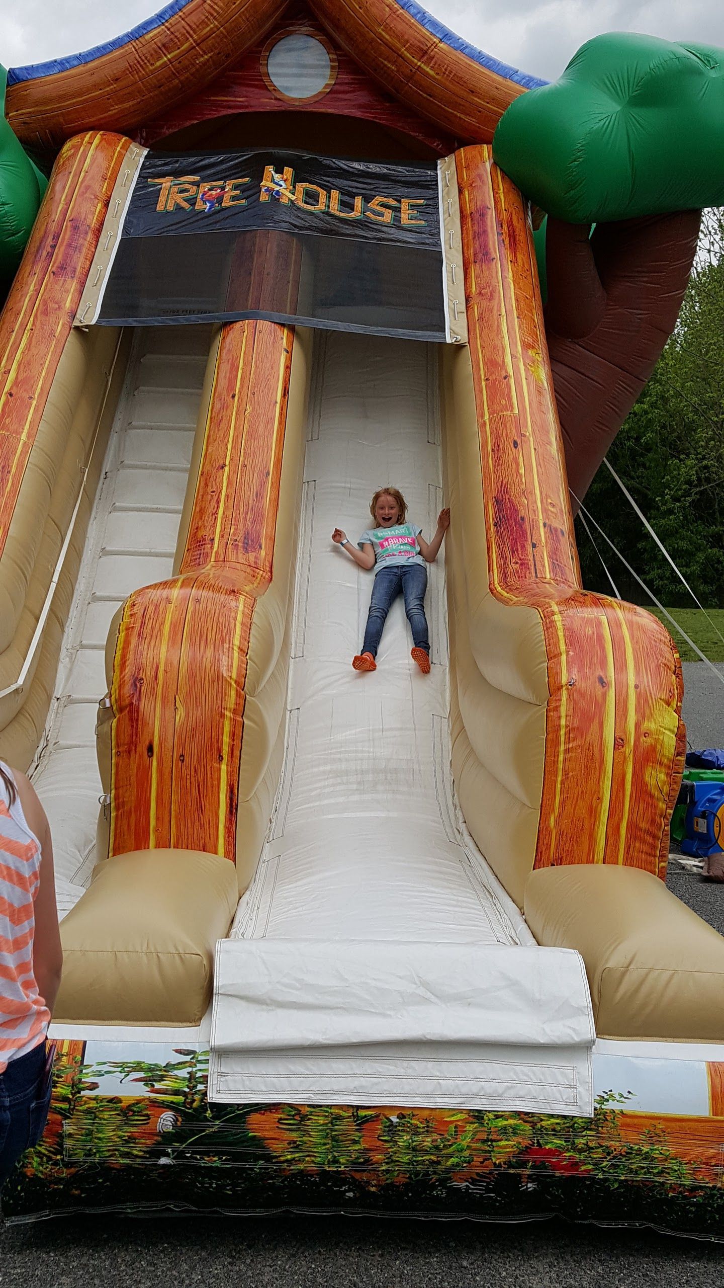 A person slides down a giant, tree-themed inflatable slide at an outdoor event.