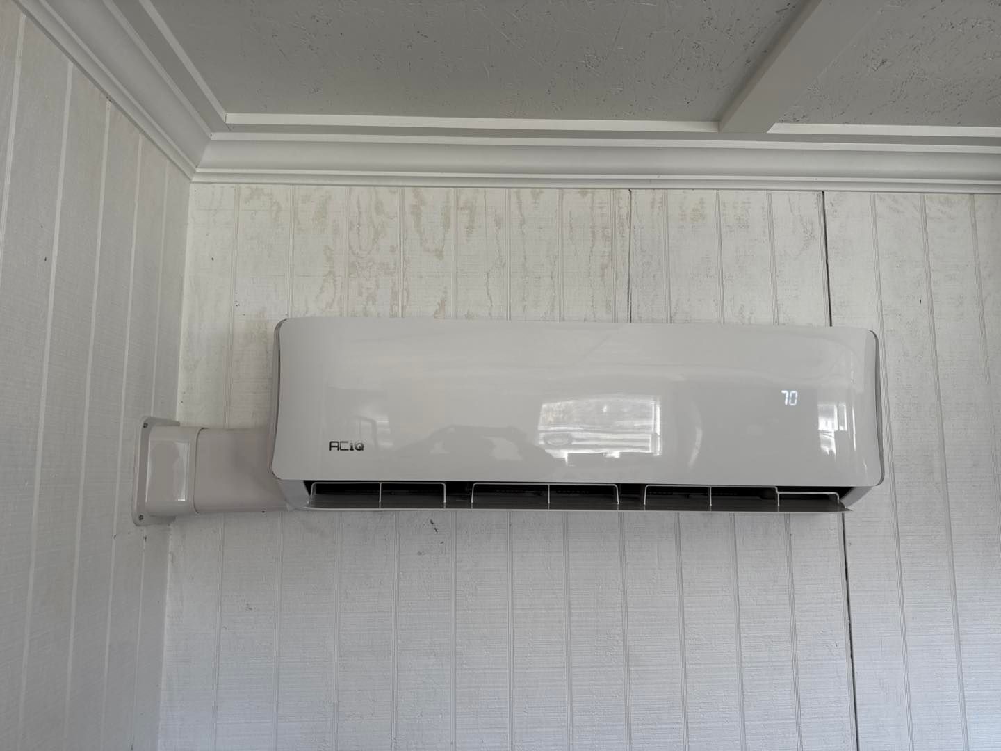 A white wall-mounted air conditioner unit installed on a white wood-paneled wall.
