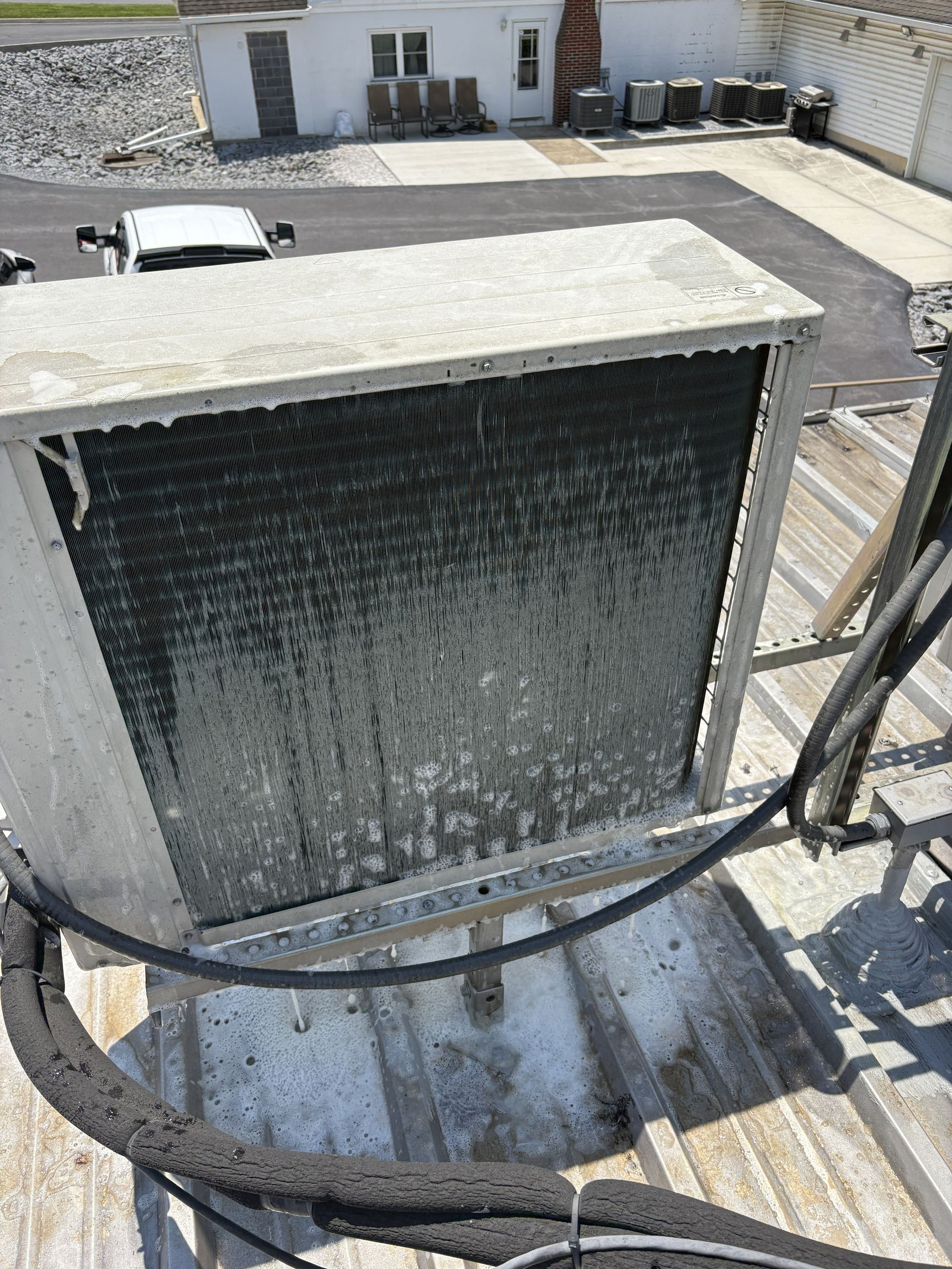 A large, rectangular HVAC condenser unit sits on a metal roof, showing a dirty, dark gray exterior coil.