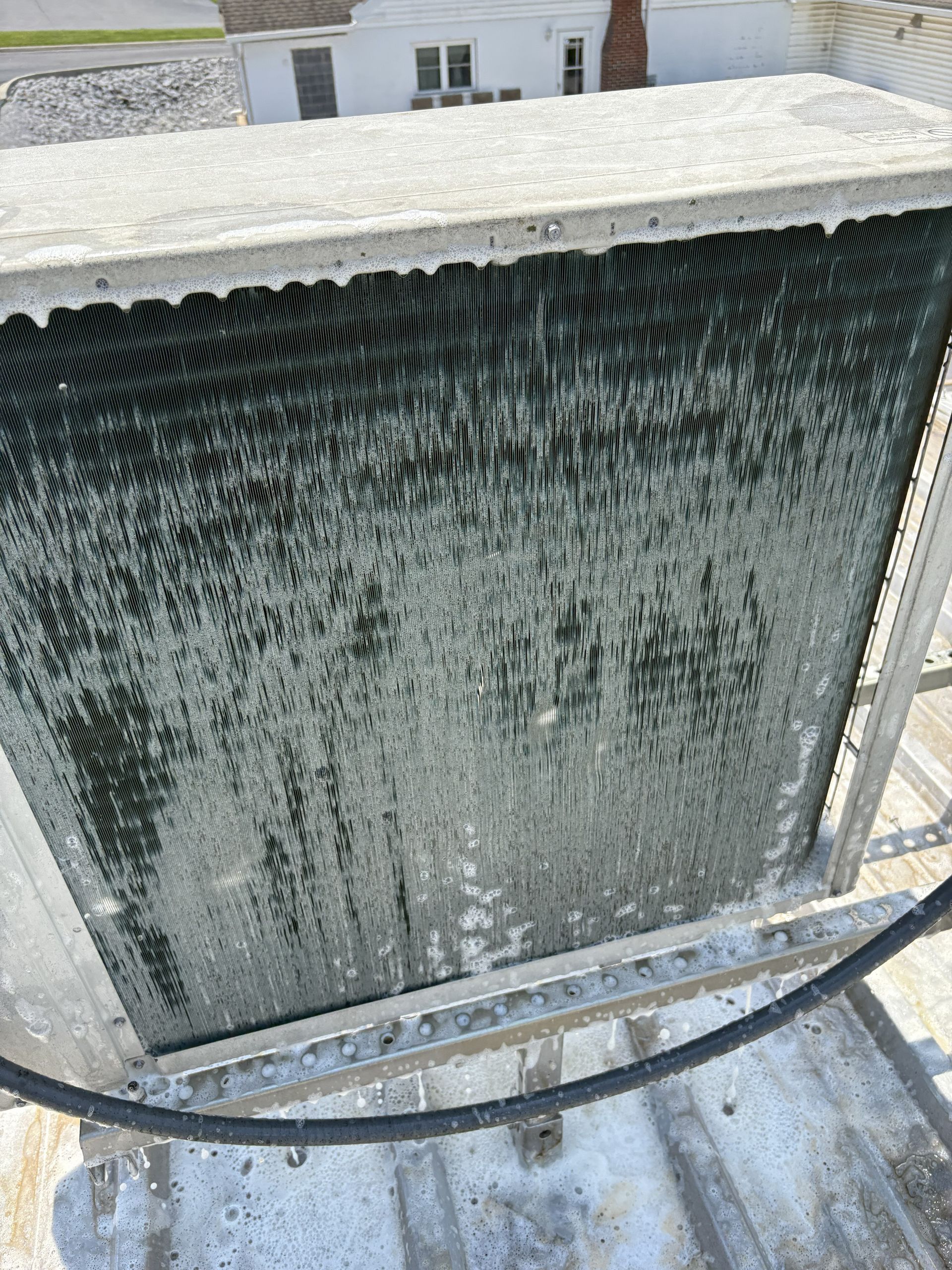 A rectangular HVAC condenser coil covered in a thick layer of grey, matted dust and debris, seen from a high angle.