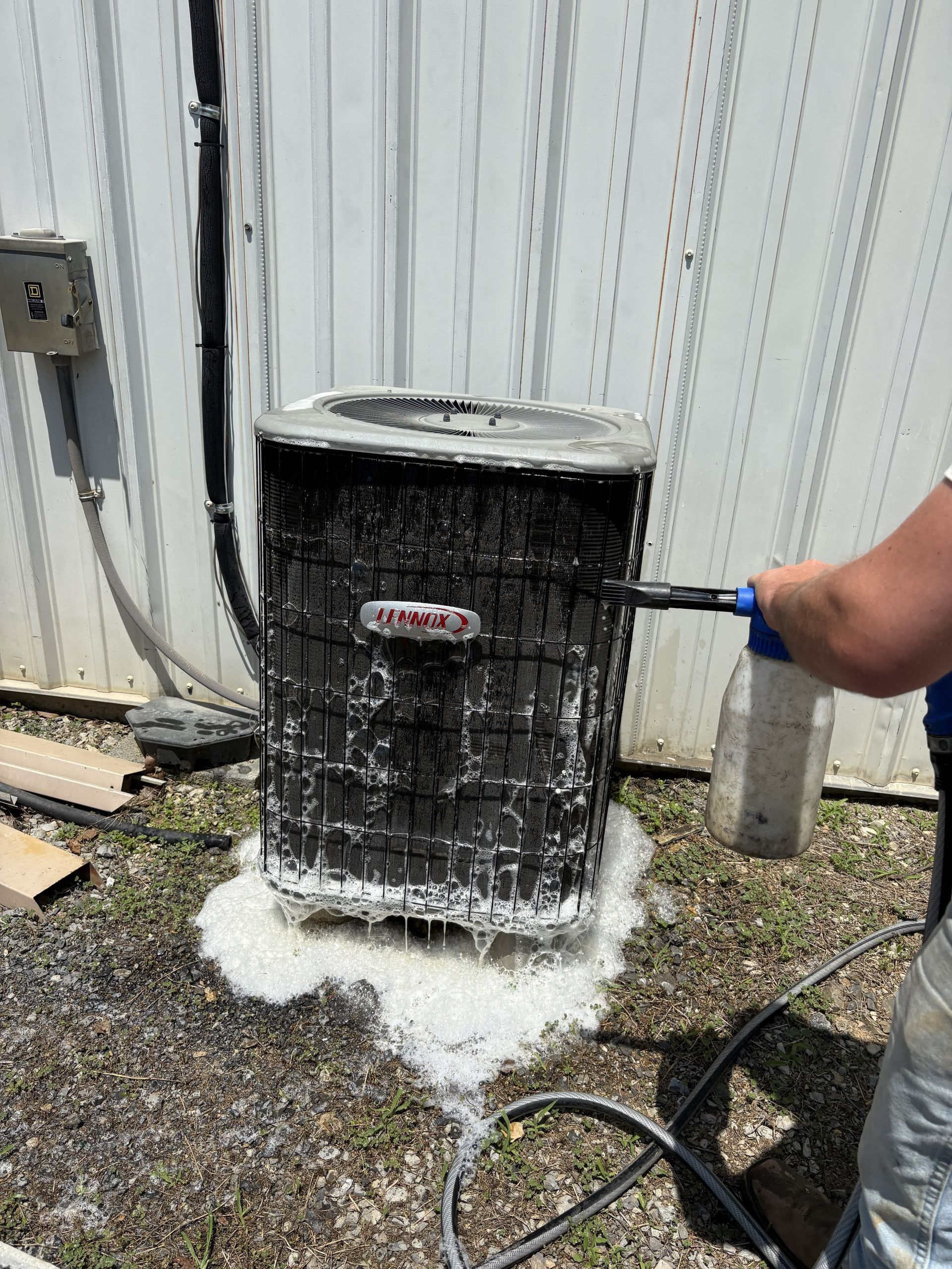 A gray HVAC air handler unit standing in a basement, connected to a drain line and condensate pump.
