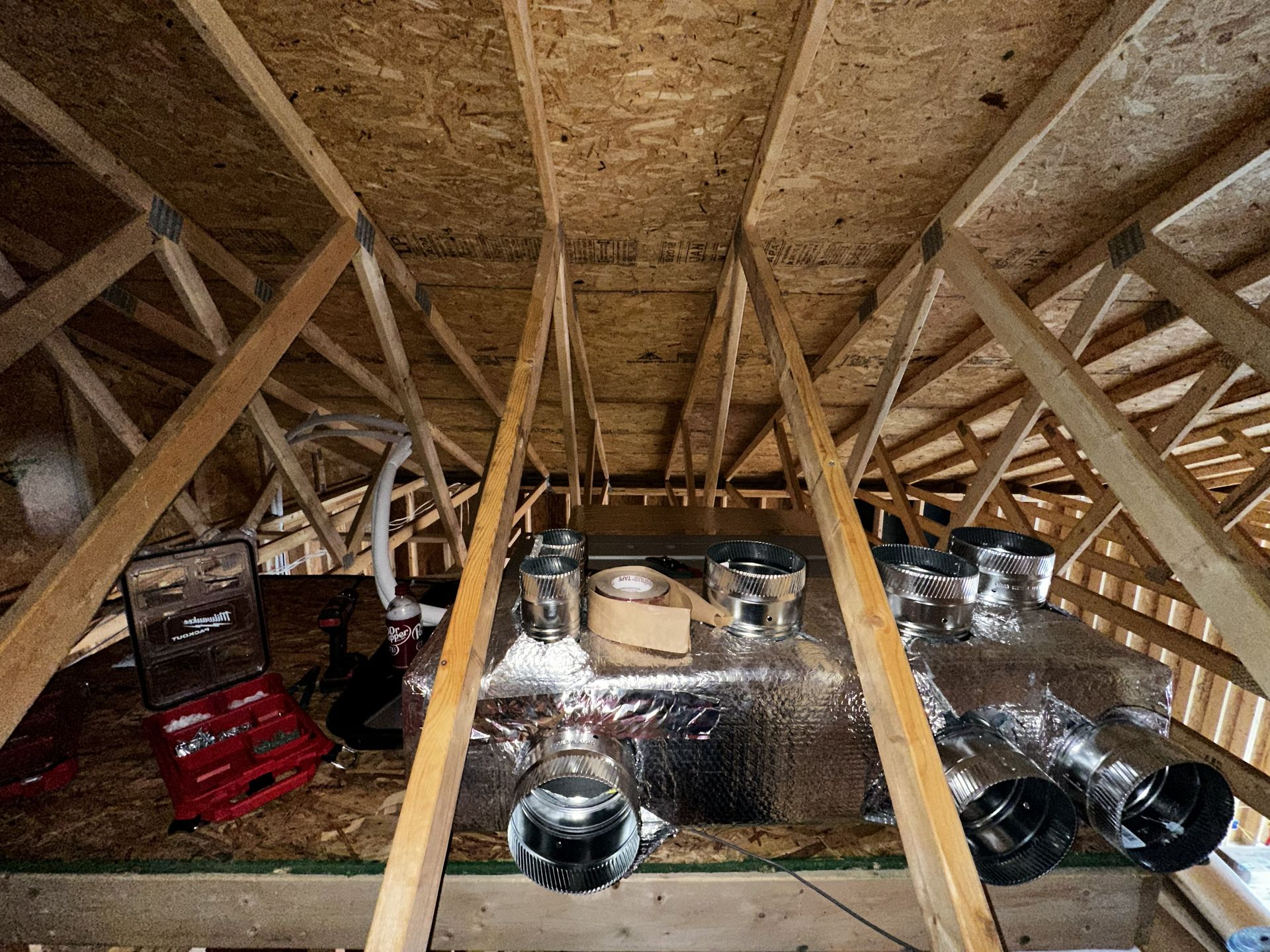 Unfinished attic space with wooden roof trusses, exposed plywood, and a large central HVAC unit with silver ductwork.