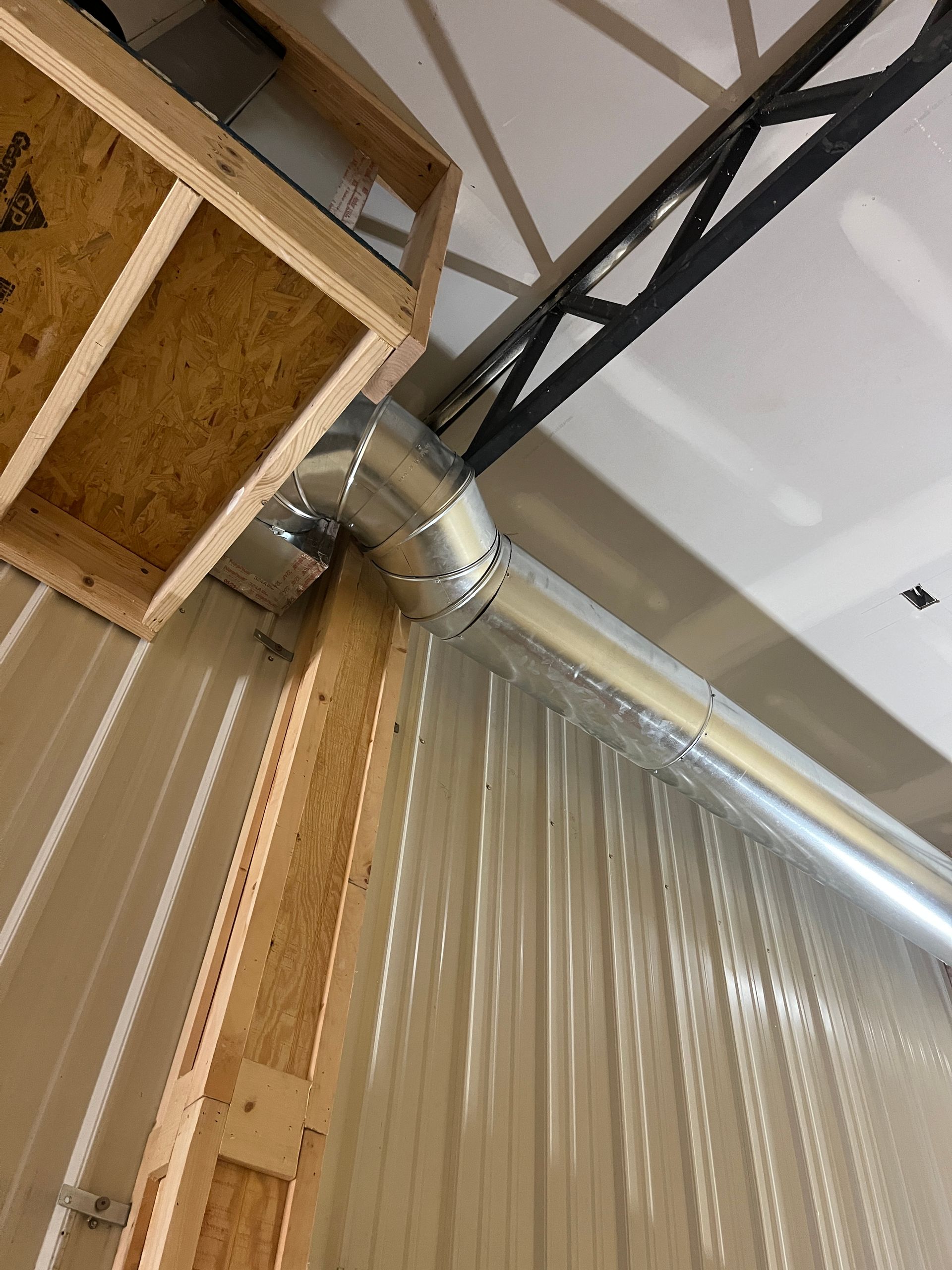 Metal ductwork runs along the corner of an interior wall beneath an exposed wooden rafter and a white ceiling.
