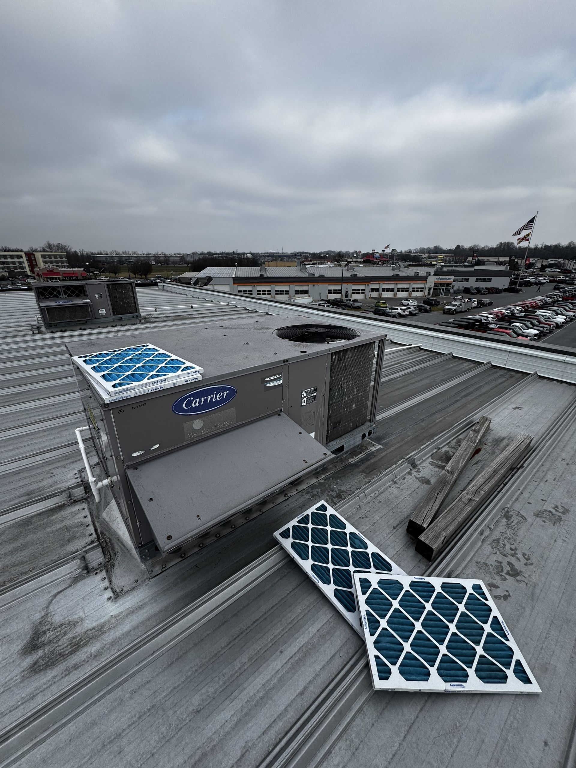 A Carrier HVAC rooftop unit with its filter access panels open, with two replacement blue air filters resting on the roof.