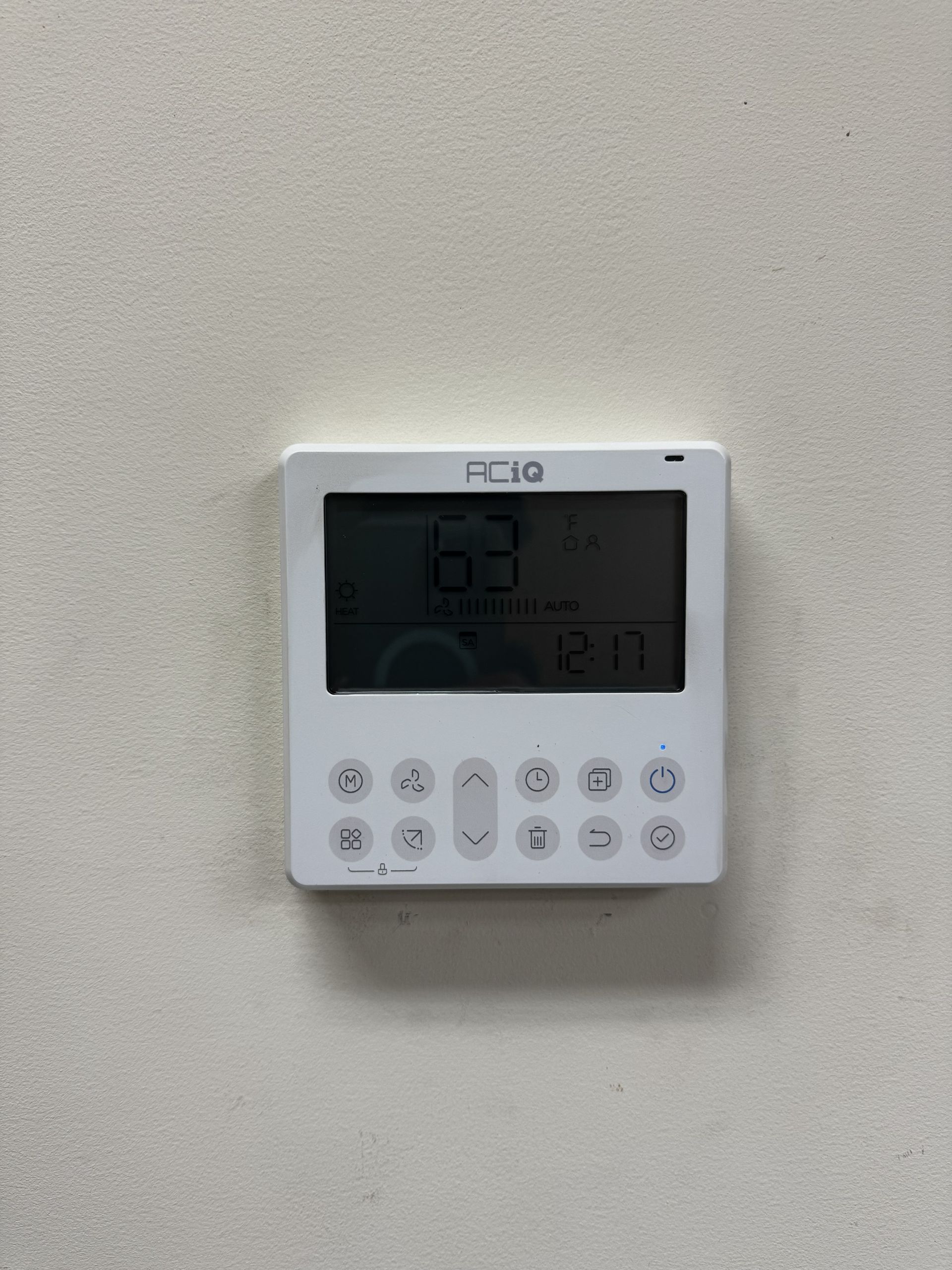 White digital wall-mounted thermostat with an LCD screen displaying 