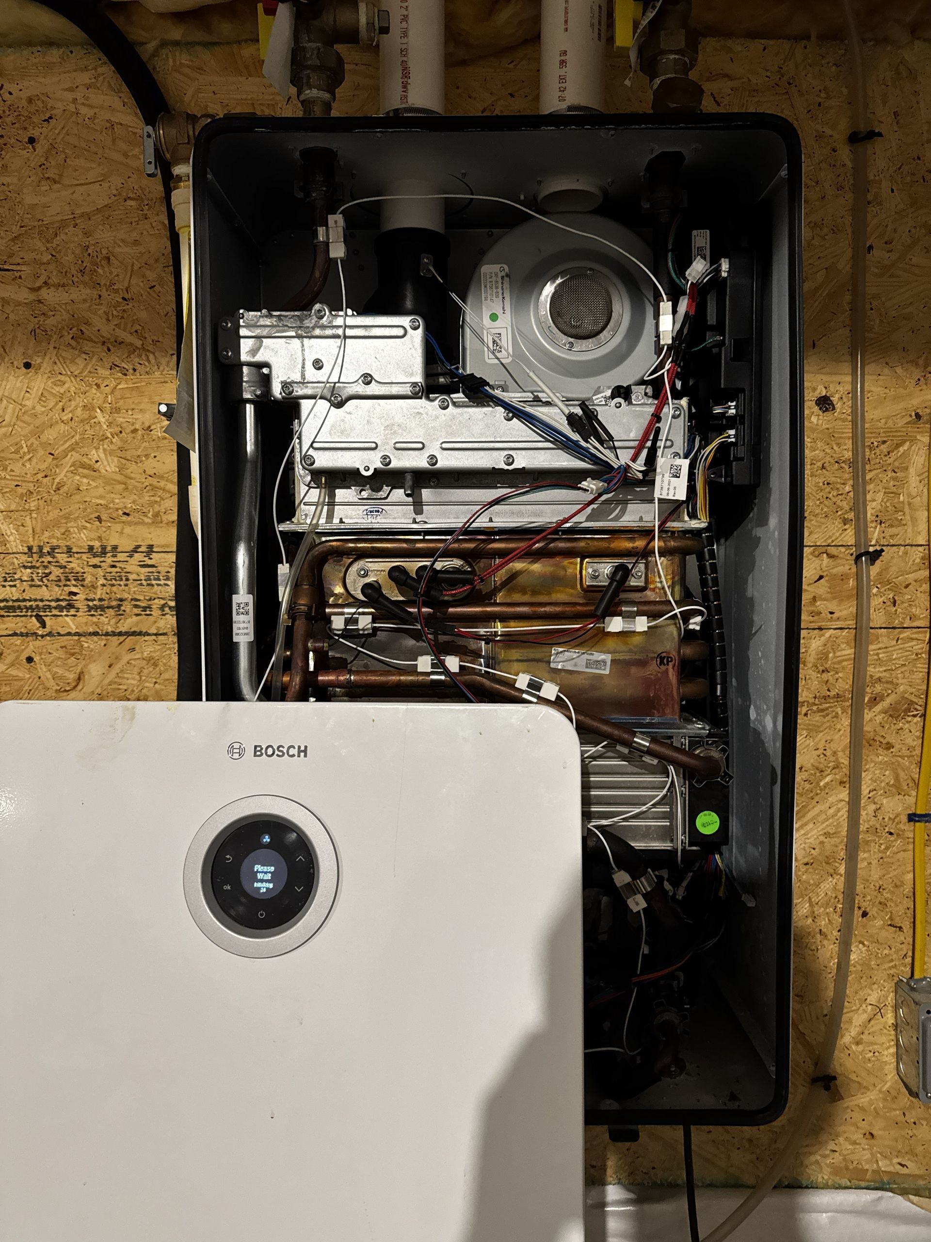 A wall-mounted Bosch tankless water heater with its front panel open, revealing internal components and piping.