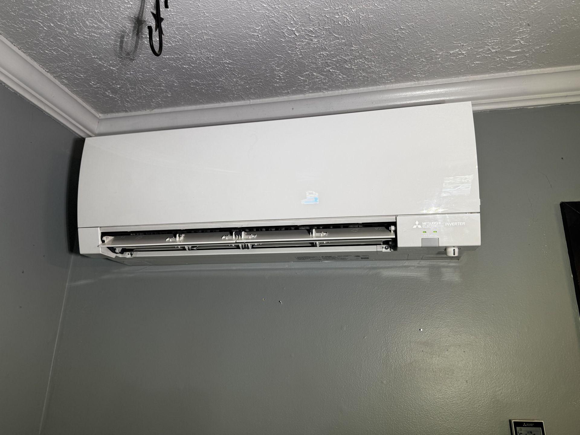 A white wall-mounted mini-split air conditioning unit installed in the corner of a room with gray walls.