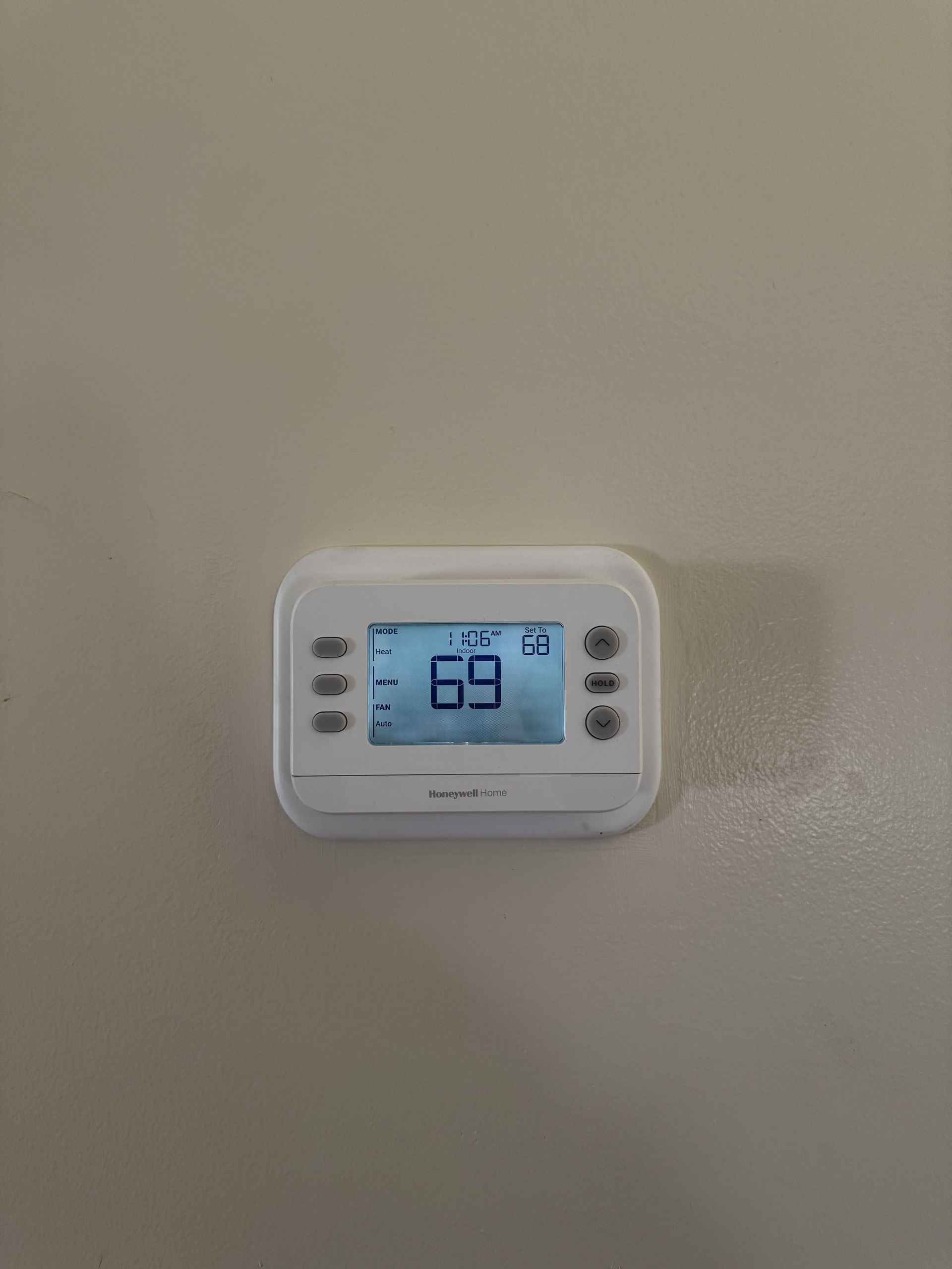 A white digital thermostat mounted on a plain wall, displaying a temperature of 69 degrees.