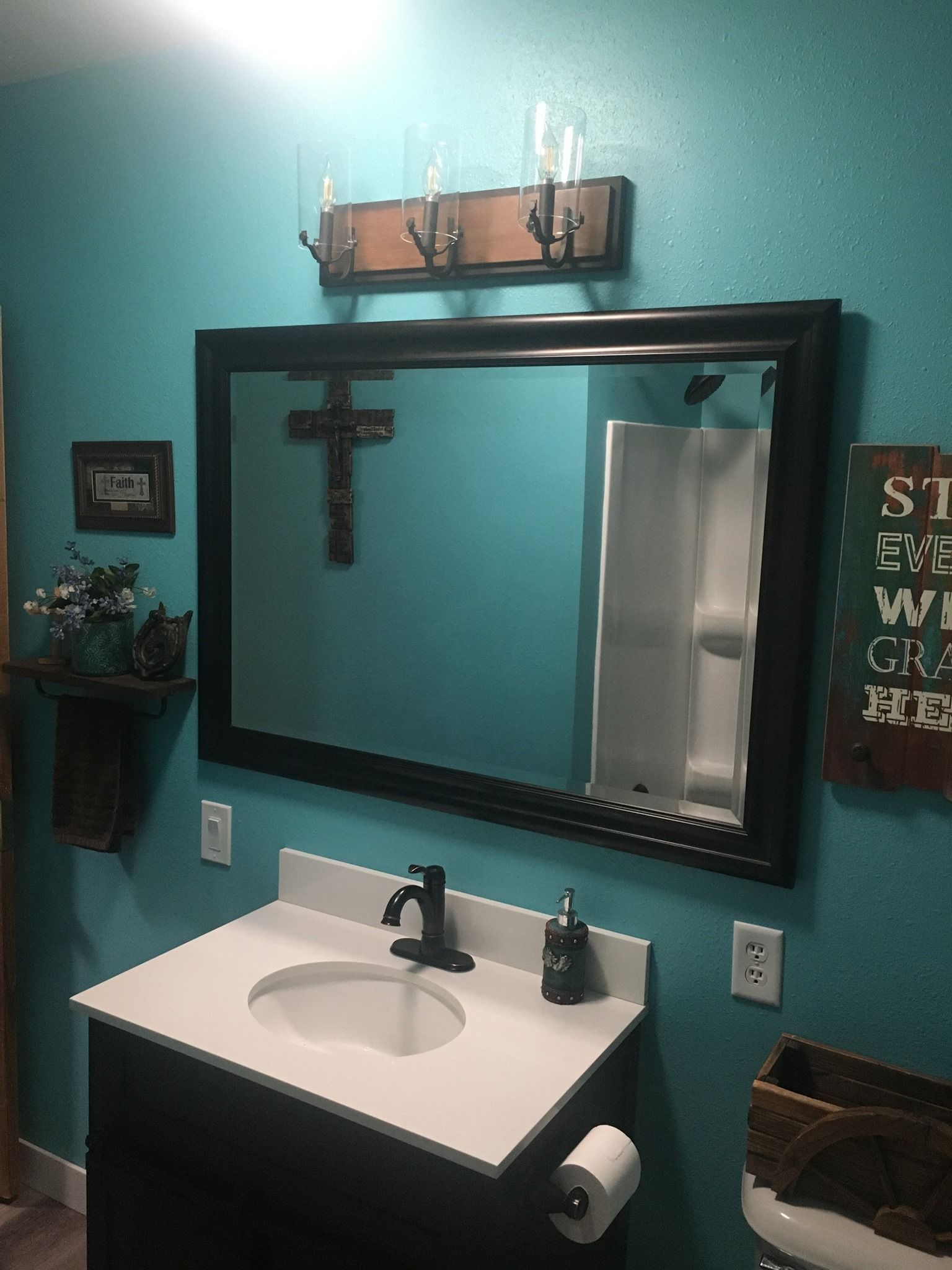 A bathroom with a sink , mirror and a cross on the wall.