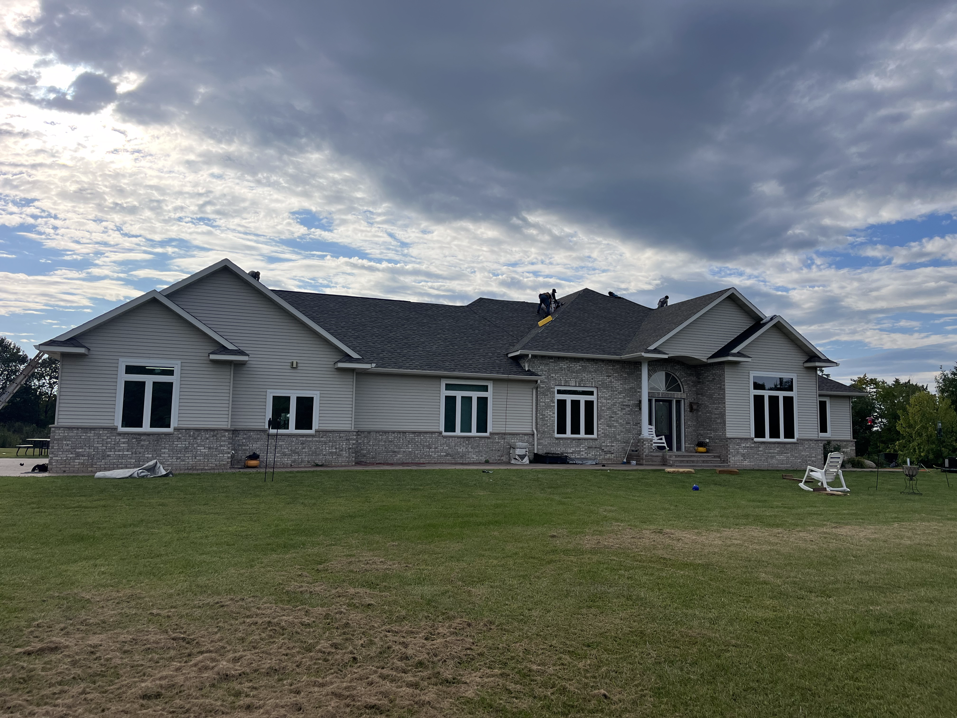 A large white house with a gray roof is sitting on top of a lush green field.