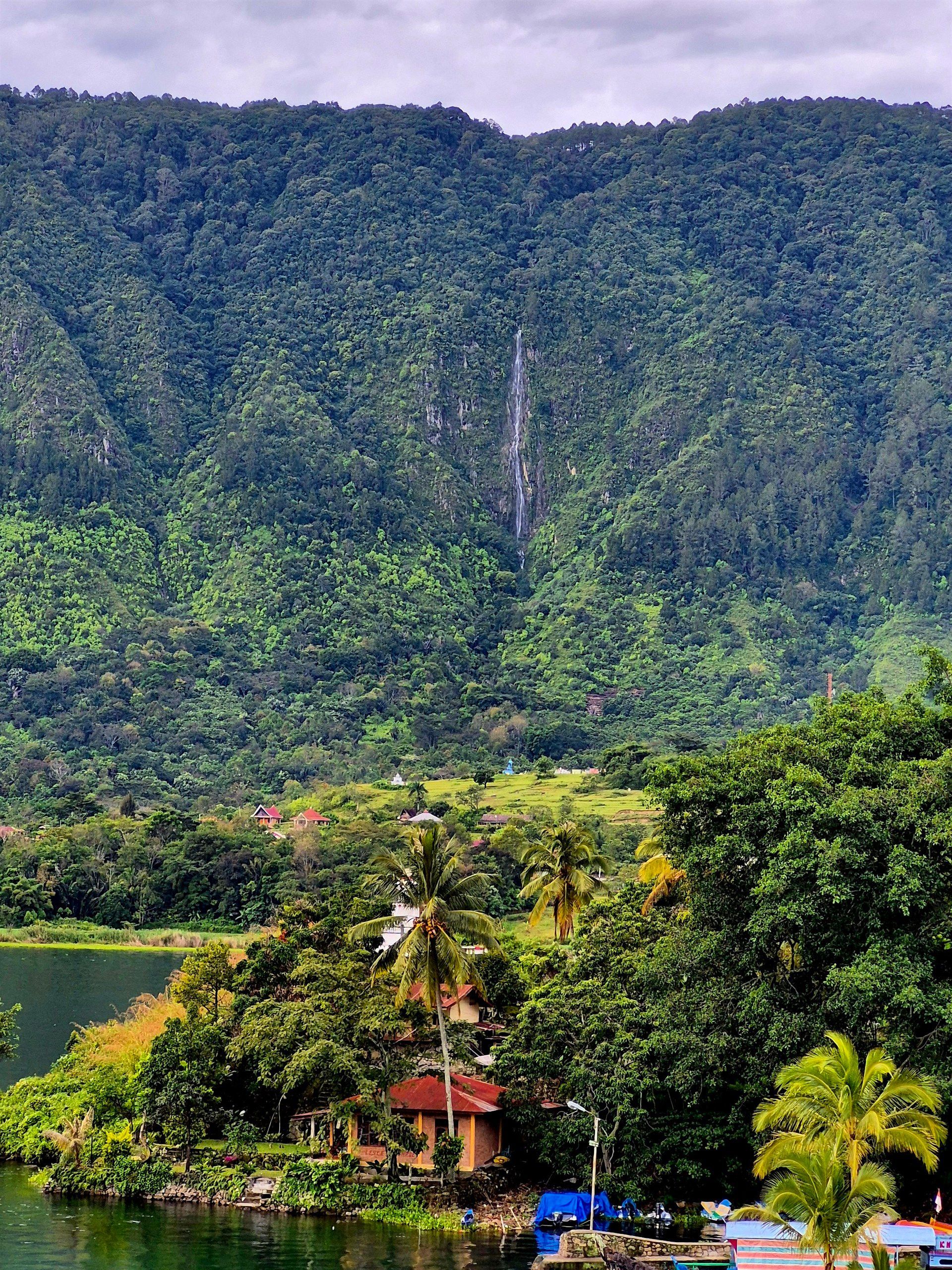 A small island in the middle of a lake with a waterfall in the background.